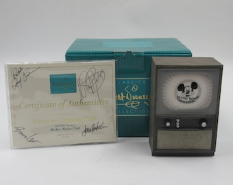 Può includere: Un set della collezione Disney Classics 50° anniversario con un televisore in stile vintage, un certificato di autenticità e una scatola color verde acqua. Il televisore ha un'immagine di Mickey Mouse Newsreel sullo schermo.