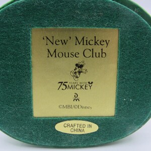 May include: A green, circular base with a gold rectangular plaque featuring the text "'New' Mickey Mouse Club" and "75 Years with Mickey". The base also has a small, oval sticker that reads "Crafted in China".