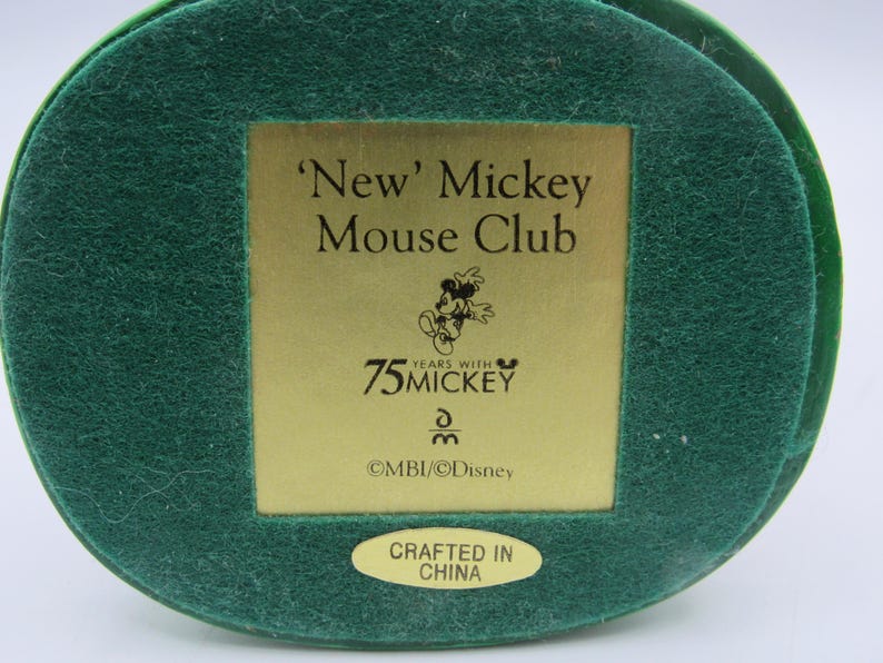 May include: A green, circular base with a gold rectangular plaque featuring the text "'New' Mickey Mouse Club" and "75 Years with Mickey". The base also has a small, oval sticker that reads "Crafted in China".