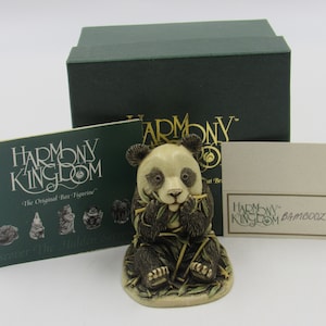 May include: A small, cream-coloured figurine of a panda bear sitting and eating bamboo. The figurine is part of the Harmony Kingdom collection and is in its original box. The box is green with gold lettering that reads "Harmony Kingdom".