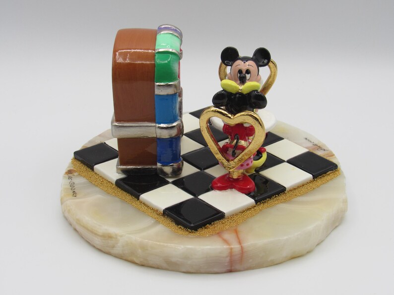 K&ouml;nnte beinhalten: Dekorative Figur mit einem braunen, blauen und gr&uuml;nen Jukebox-Design, mit einer Mickey Mouse Figur, die ein goldenes Herz h&auml;lt. Die Figur steht auf einer schwarz-wei&szlig; karierten Basis mit goldenem Rand, auf einer runden, cremefarbenen Steinbasis.