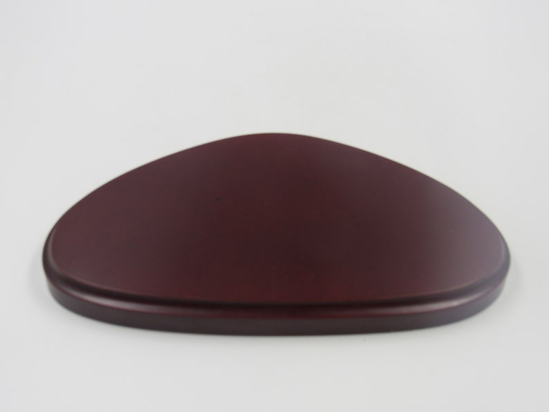 May include: A dark red wooden display stand shaped like an oval. The stand is smooth and has a slightly rounded edge.