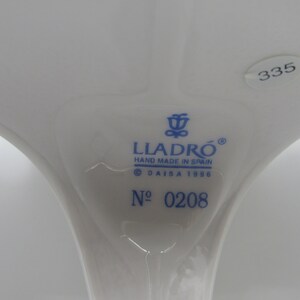 May include: A white porcelain figurine with blue markings. The figurine is marked with the Lladro logo, "Hand Made in Spain", "DAISA 1986", and "N&deg; 0208".