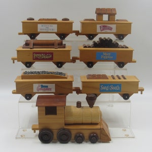 May include: A wooden toy train set with a locomotive and six cars. The cars are decorated with various Disney movie themes, including "Pete's Dragon", "Mary Poppins", "Song of the South", and "Runaway Brain".