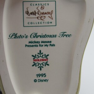 May include: A close-up of a white ceramic collectible featuring text that reads "Pluto's Christmas Tree" and "Mickey Mouse Presents for My Pals." The design includes a snowflake and the year 1995, with the Disney logo. The item is part of the "Walt Disney Collection."