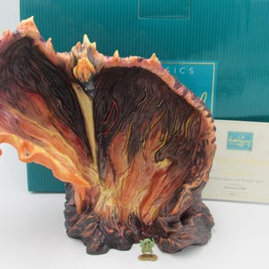 Può includere: Una statuetta dettagliata e dipinta a mano di un'eruzione vulcanica ardente, arancione e rossa, con una piccola statuetta verde in piedi di fronte ad essa. La statuetta fa parte di una collezione chiamata "Disney's Imagineering Collection".