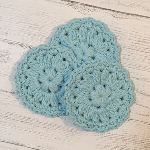 May include: Three crocheted light blue coasters with a flower design.
