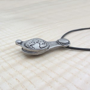 May include: A silver pendant necklace with a globe design. The pendant is attached to a black cord.