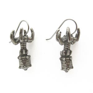 May include: A pair of silver lobster earrings with a detailed design. The earrings are made of metal and have a lobster claw design.