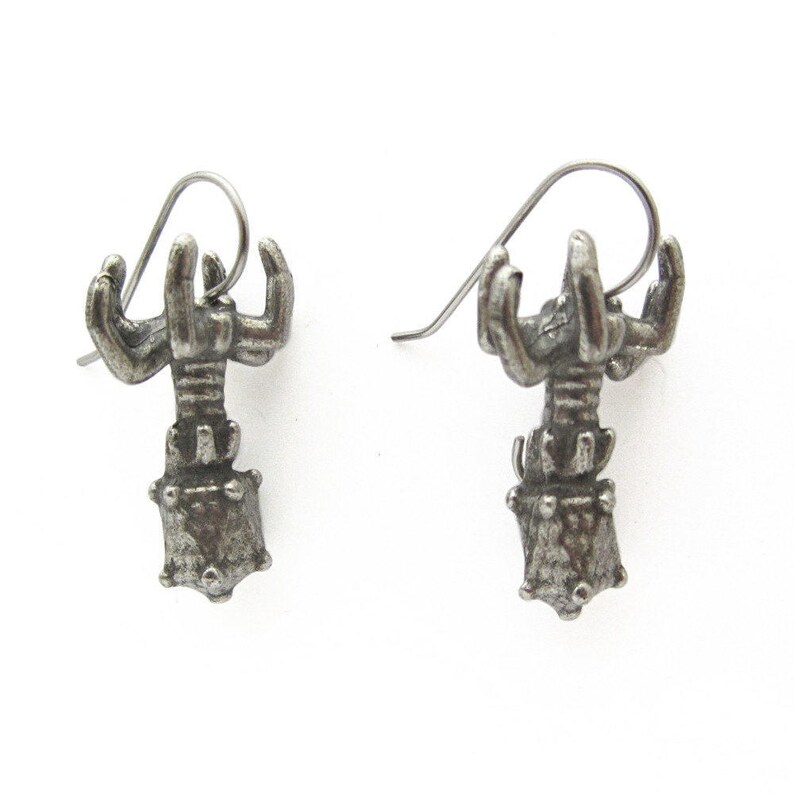 May include: A pair of silver lobster earrings with a detailed design. The earrings are made of metal and have a lobster claw design.