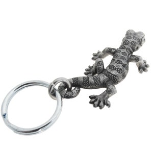 May include: A silver metal gecko keyring. The gecko has a detailed, textured body with spotted and striped patterns. The keyring includes a strong metal ring for attaching keys or accessories.