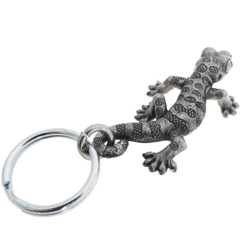 May include: A silver metal gecko keyring. The gecko has a detailed, textured body with spotted and striped patterns. The keyring includes a strong metal ring for attaching keys or accessories.