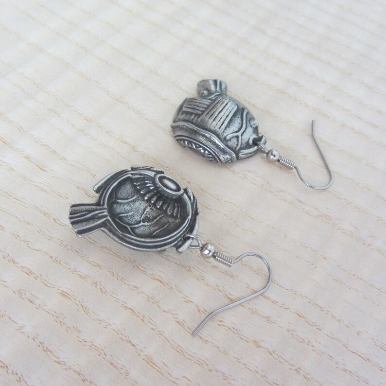 May include: A pair of silver earrings with a detailed eye design. The earrings are made of metal and have a hook closure.