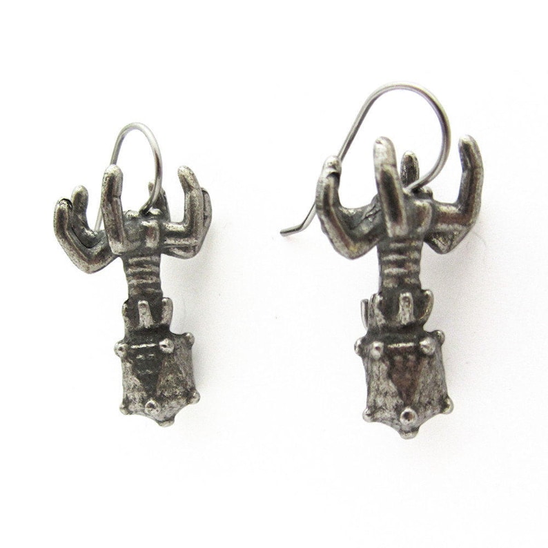 May include: A pair of silver lobster earrings with a detailed design. The lobster is in a standing position with its claws raised.