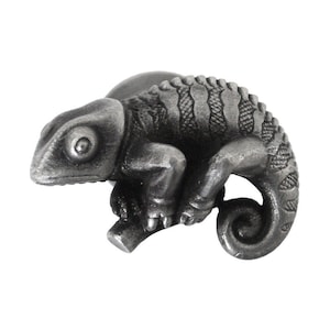 May include: A detailed, metallic chameleon figurine in a seated pose. The reptile is a muted gray color, with textured skin and a curled tail. It is perched on a small branch, showcasing its intricate design.