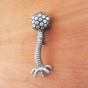 May include: Silver cabinet knob with a hexagonal patterned top and a curved stem ending in a three-pronged foot.