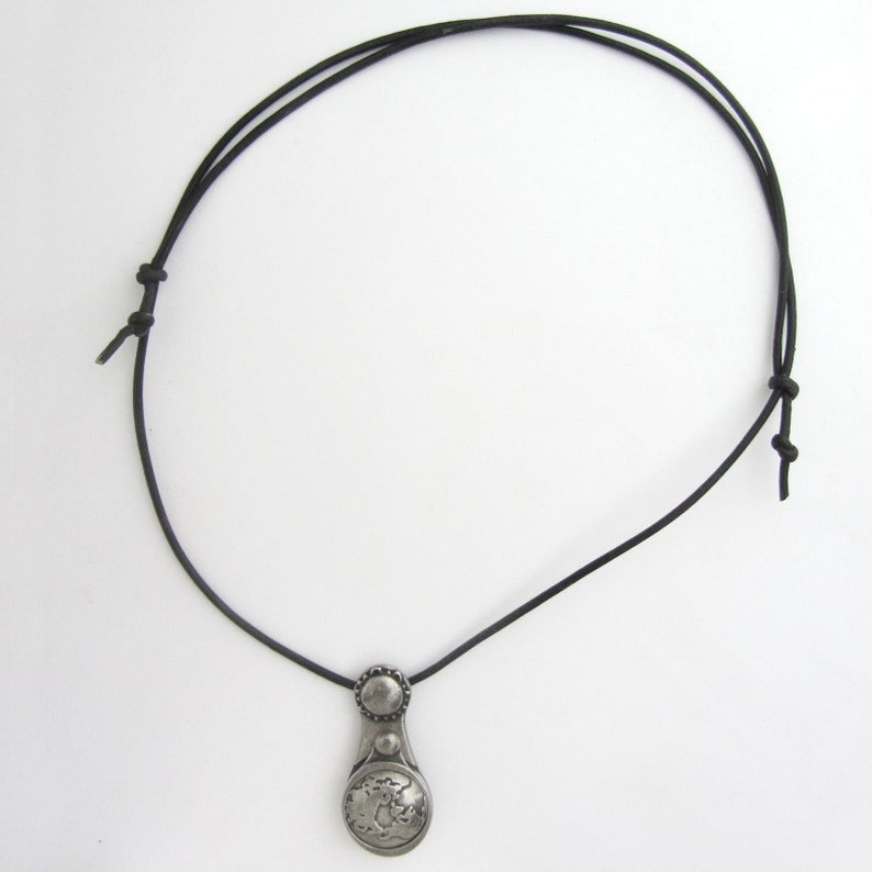 May include: A silver pendant necklace with a round, detailed design hangs from a black leather cord.