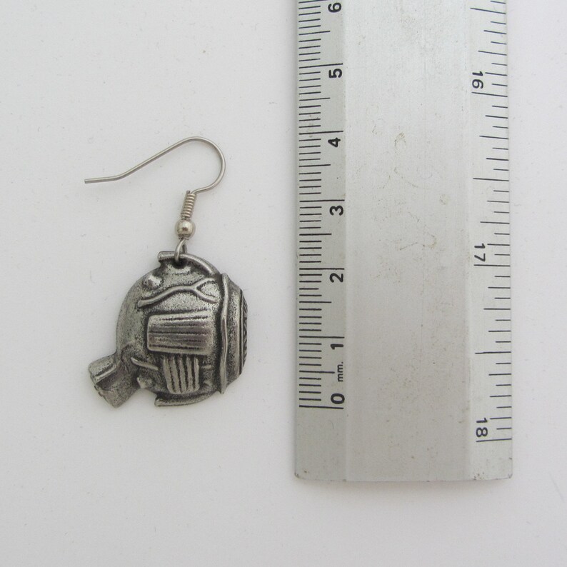 May include: Silver tone fish shaped earrings with a detailed design. The earrings are approximately 2 cm in length.