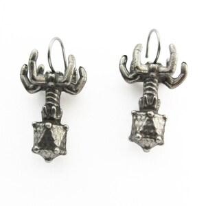 May include: A pair of silver earrings featuring a detailed design of a creature with multiple arms holding a geometric shape.