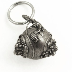 May include: A detailed, silver-colored keychain charm. The charm is a rounded, textured shape with intricate, raised designs and a small loop for attaching to a keyring. The keyring is a simple, circular design.