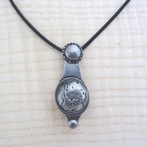 May include: A silver pendant necklace with a detailed globe design. The pendant is attached to a black cord.