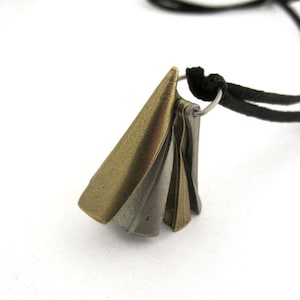 May include: A pendant necklace featuring a cluster of metallic cone-shaped charms in bronze and silver tones. The charms are attached to a silver ring and suspended from a black cord. The necklace is displayed against a white background.