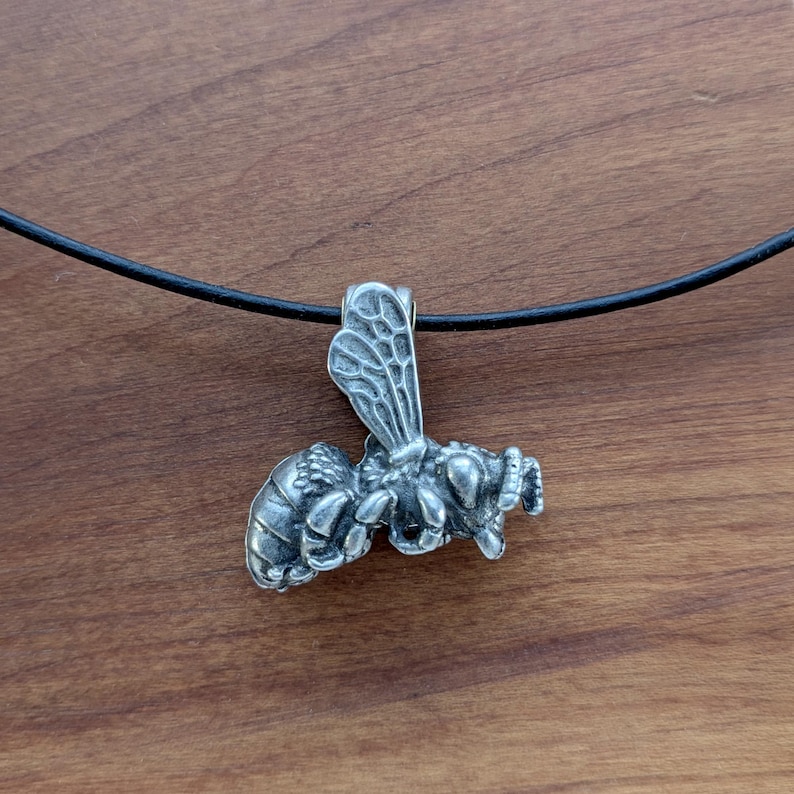 May include: A silver bee pendant necklace with a black cord. The bee is detailed and has wings, legs, and a stinger.