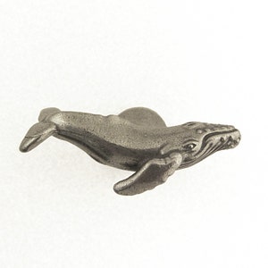 May include: A detailed, pewter-colored whale figurine. The whale is depicted in a swimming pose, with its flippers extended. The figurine has textured details, including the whale's eye, mouth, and body ridges. The whale is approximately 4 inches long.
