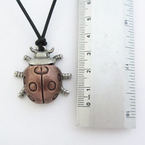 May include: A ladybug pendant necklace with a black cord. The ladybug pendant is made of metal with a copper-colored body and silver-colored head and legs. The pendant measures approximately 1.5 inches in length.