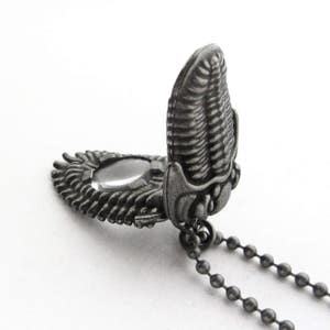 May include: A silver-toned necklace with a pendant shaped like a trilobite fossil. The pendant opens to reveal a small mirror inside.