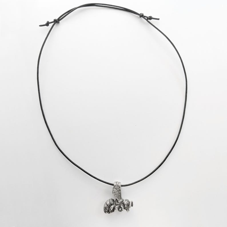May include: A silver bee pendant necklace on a black leather cord.