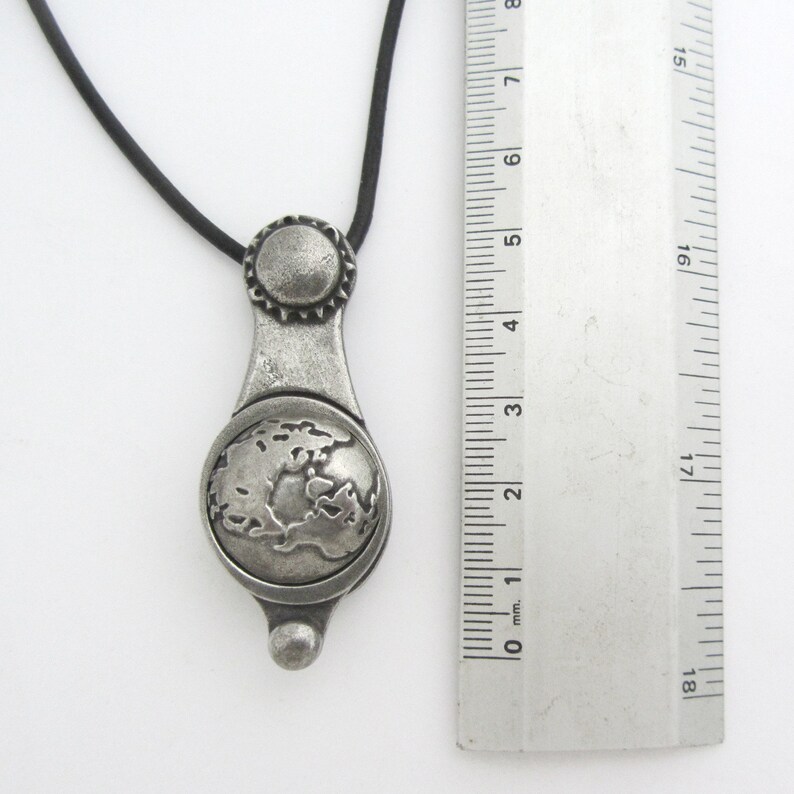 May include: A silver pendant necklace with a globe design. The pendant is attached to a black cord.