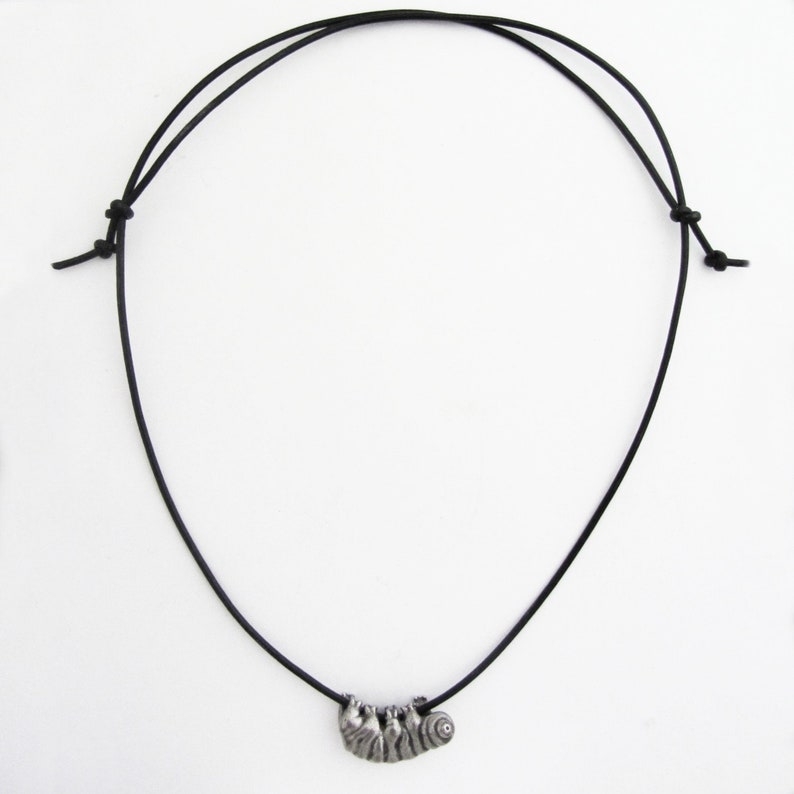 May include: A black cord necklace featuring a silver-toned pendant shaped like a sloth. The sloth pendant has detailed etched lines and is suspended from the adjustable cord. The necklace is displayed against a white background.
