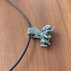 May include: A silver bee pendant on a black cord necklace. The bee is detailed with wings and legs.