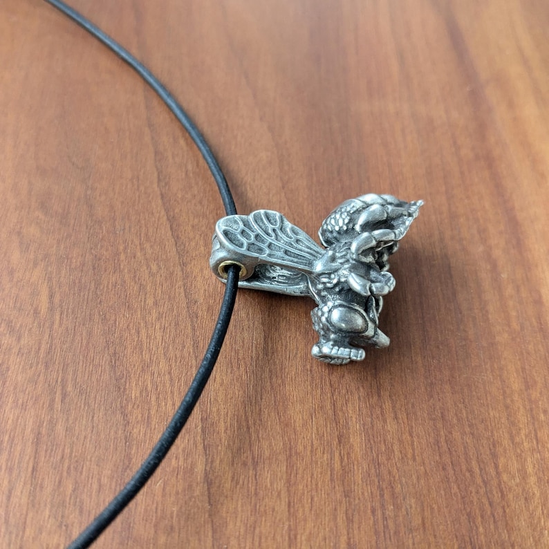 May include: A silver bee pendant on a black cord necklace. The bee is detailed with wings and legs.