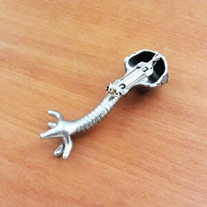 May include: Silver-toned brooch shaped like a stylized anatomical heart with a detailed design. The brooch has a pin and catch closure on the back.