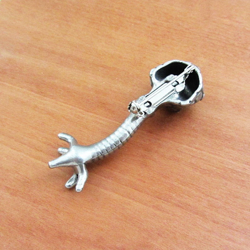 May include: Silver-toned brooch shaped like a stylized anatomical heart with a detailed design. The brooch has a pin and catch closure on the back.