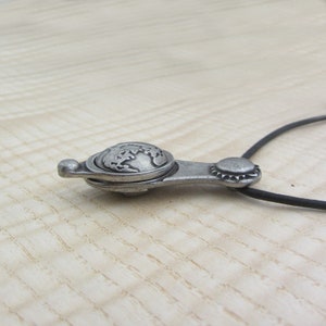 May include: A silver necklace with a globe pendant. The pendant is detailed with a raised globe design and has a hinged opening.