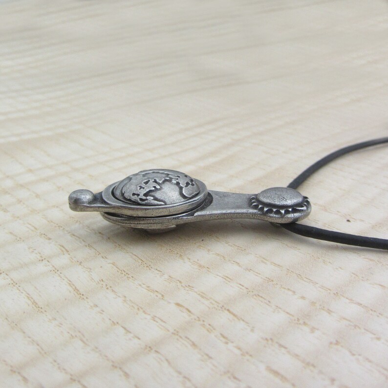 May include: A silver necklace with a globe pendant. The pendant is detailed with a raised globe design and has a hinged opening.