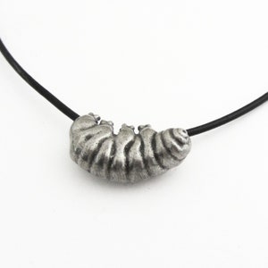 May include: A silver-toned caterpillar pendant necklace. The caterpillar has detailed ridges and is strung on a black cord. The necklace is set against a white background.