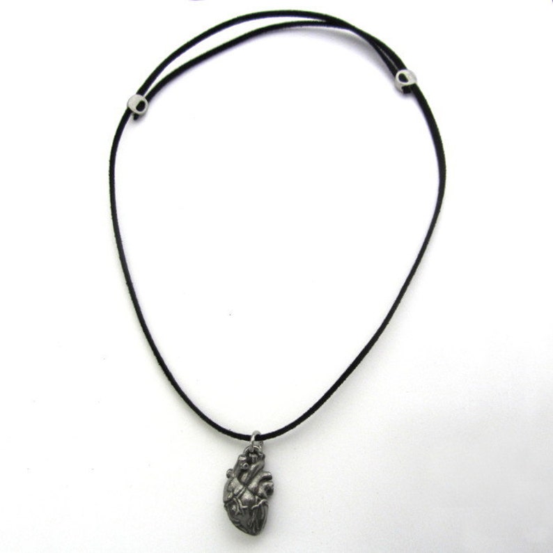 May include: A silver anatomical heart pendant on a black cord necklace.