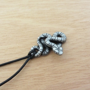 May include: A silver snake pendant necklace with a black leather cord. The snake is coiled and has a detailed design.