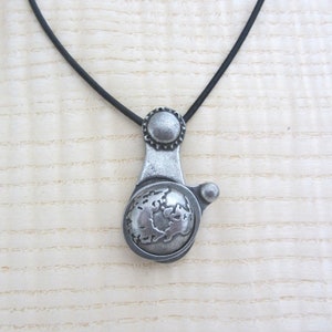 May include: A silver necklace with a globe pendant. The globe is detailed with continents and oceans. The necklace is on a black cord.