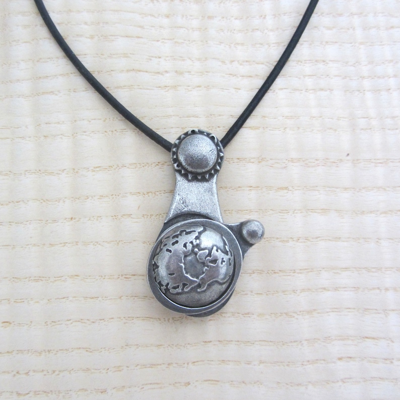 May include: A silver necklace with a globe pendant. The globe is detailed with continents and oceans. The necklace is on a black cord.