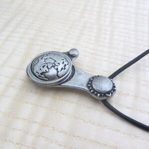 May include: A silver pendant necklace with a globe design. The pendant is attached to a black cord.