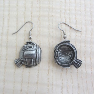 May include: A pair of silver earrings shaped like a human eye. The earrings are detailed with the internal structures of the eye, including the iris, pupil, and lens.
