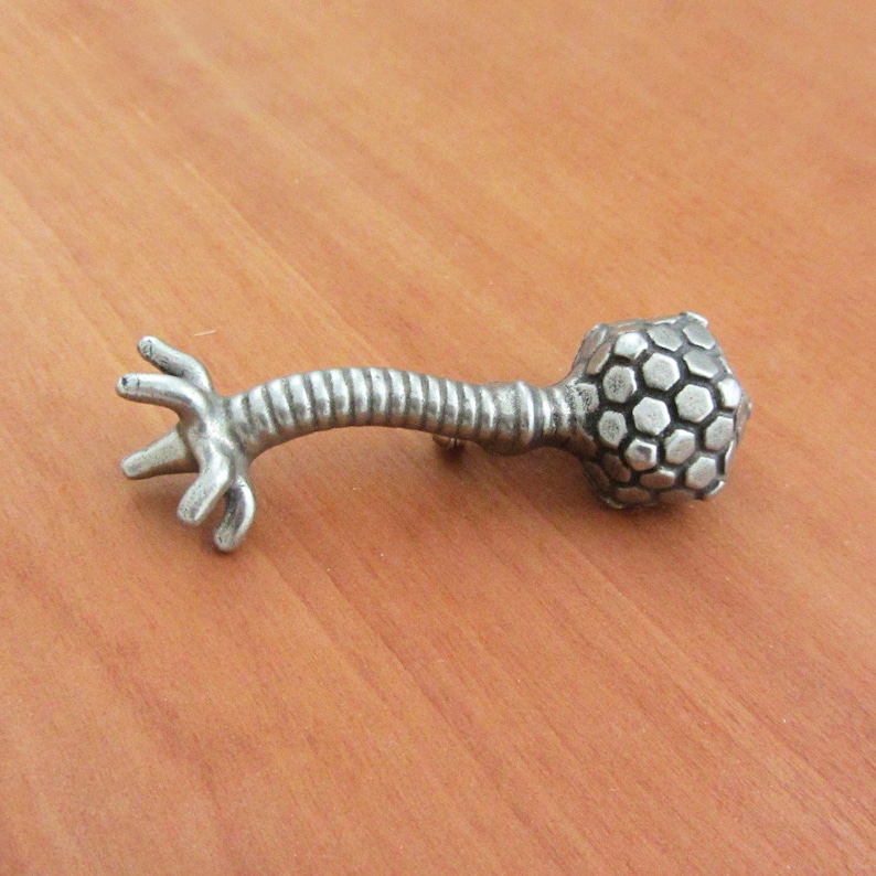 May include: A silver-toned metal pin shaped like a neuron with a hexagonal patterned head.
