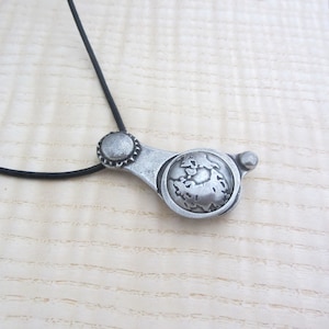 May include: A silver necklace with a pendant shaped like a globe. The pendant is detailed with a textured globe design and a small, circular accent at the top.