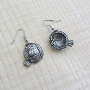 May include: A pair of silver earrings shaped like a human eye. The earrings are detailed with the internal anatomy of the eye, including the iris, pupil, and optic nerve.
