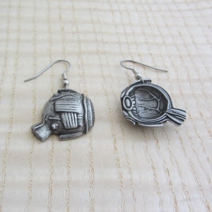 May include: A pair of silver earrings shaped like a fish with a detailed design. The earrings are hanging from silver hooks.